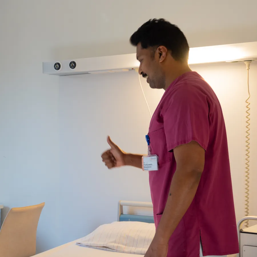 Pfleger in Dienstkleidung zeigt im Patientenzimmer den Daumen nach oben